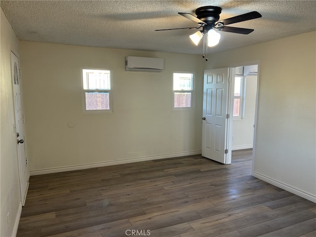spare room featuring a wall mounted air conditioner, a ceiling fan, healthy amount of natural light, dark wood-style flooring, and a textured ceiling