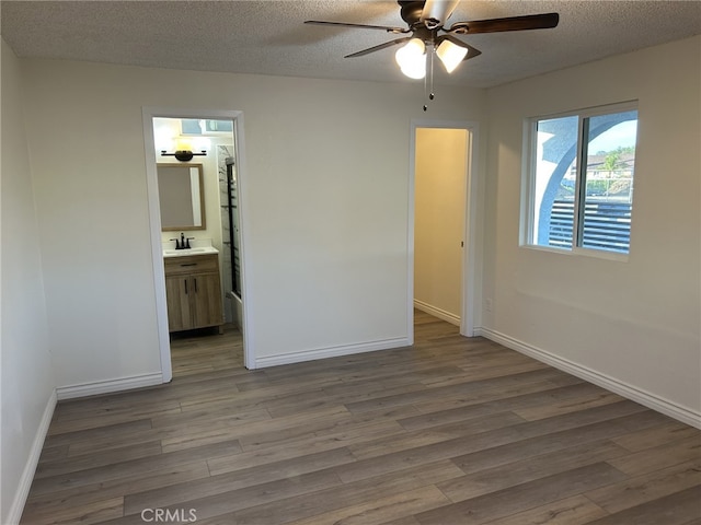 unfurnished bedroom with a sink, wood finished floors, a textured ceiling, baseboards, and ensuite bathroom