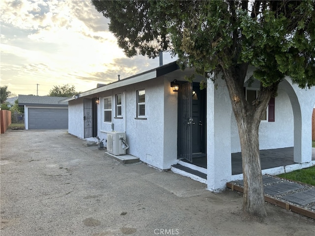 property exterior at dusk featuring stucco siding, an outdoor structure, and a detached garage