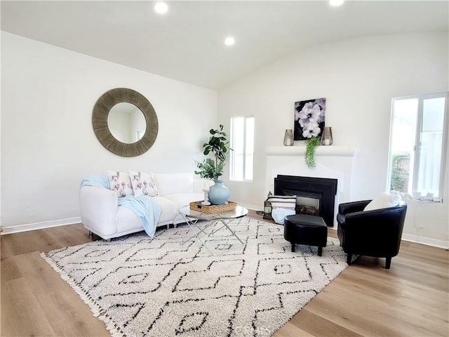 living area with a glass covered fireplace, recessed lighting, baseboards, wood finished floors, and vaulted ceiling