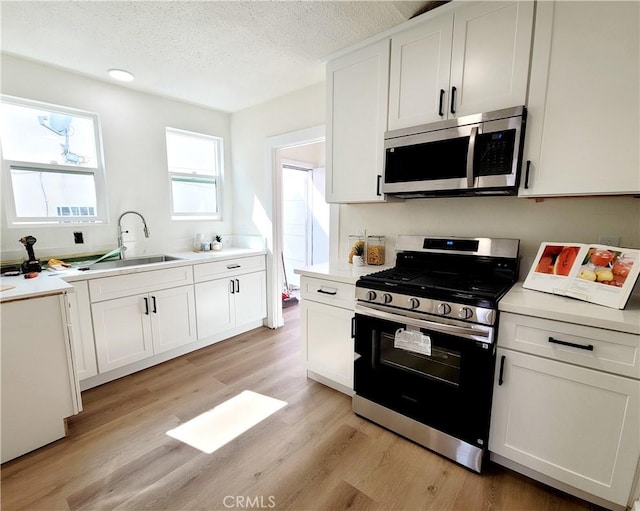kitchen with a sink, light wood-style floors, light countertops, stainless steel appliances, and white cabinetry