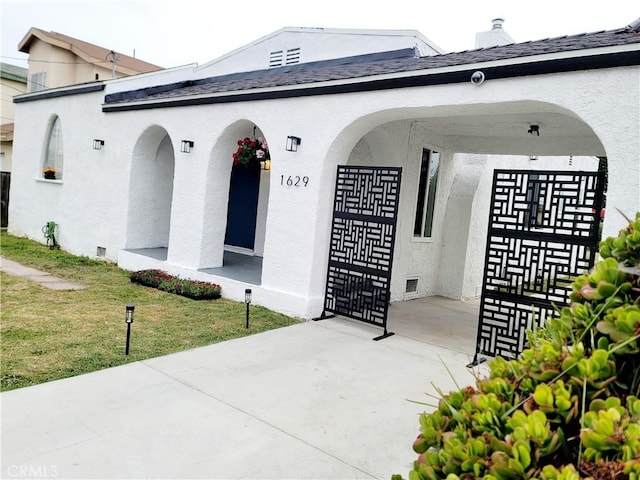 view of exterior entry with a lawn, roof with shingles, and stucco siding