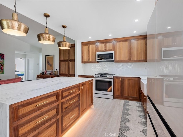 kitchen featuring brown cabinets, decorative backsplash, stainless steel gas range oven, and white microwave