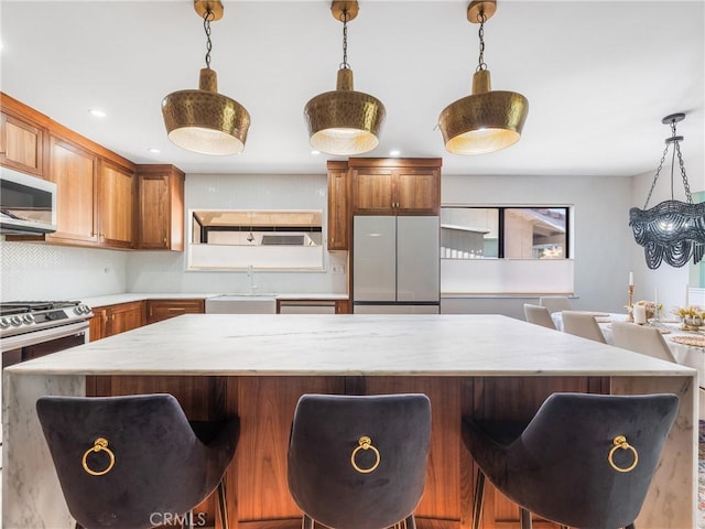 kitchen with brown cabinetry, a kitchen bar, hanging light fixtures, a sink, and stainless steel appliances