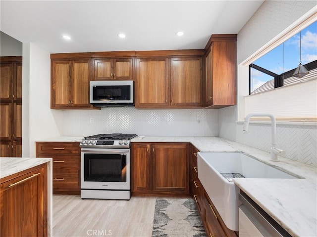 kitchen with decorative backsplash, light stone counters, stainless steel range with gas stovetop, a sink, and light wood-style flooring