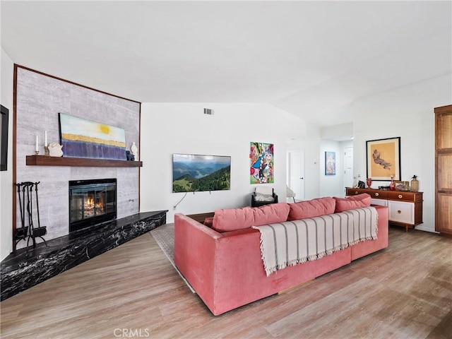 living area with visible vents, a large fireplace, wood finished floors, and lofted ceiling
