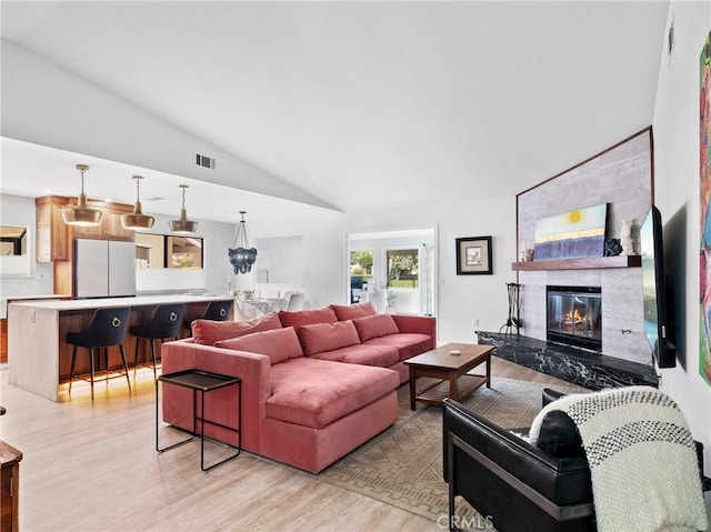 living room featuring visible vents, a large fireplace, lofted ceiling, and light wood-style floors