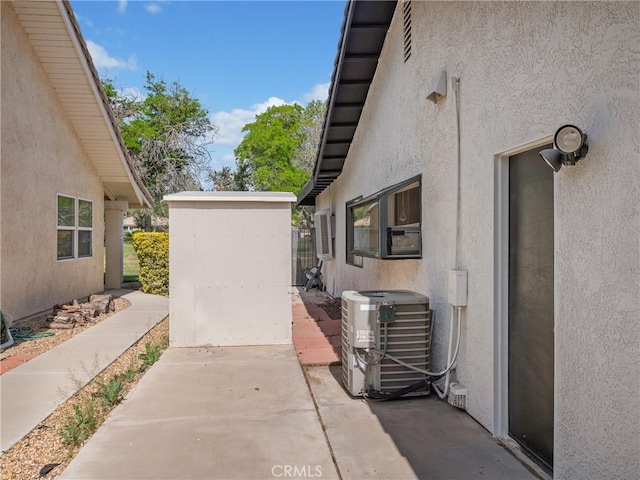 view of property exterior featuring a patio, stucco siding, central AC unit, a storage shed, and an outbuilding