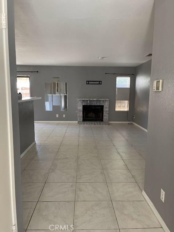 10434 Peach Ct, Adelanto, CA 92301 - unfurnished living room featuring a brick fireplace, baseboards, and light tile patterned floors