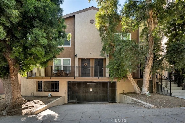 view of front of house with stairs, stucco siding, an attached garage, and driveway