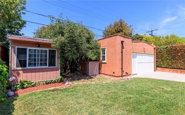 exterior space with concrete driveway, an outdoor structure, a front yard, and stucco siding