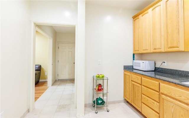 kitchen featuring light brown cabinets, baseboards, and white microwave