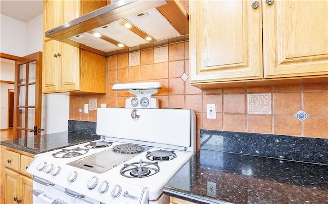 kitchen featuring dark stone countertops, wall chimney range hood, white gas range, and tasteful backsplash