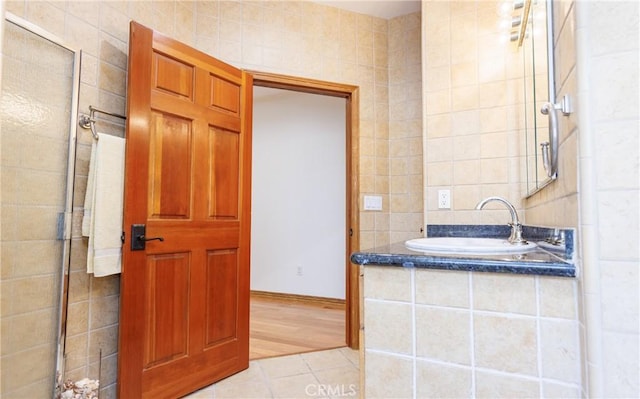 full bath with a shower with door, tile patterned floors, tile walls, and a sink
