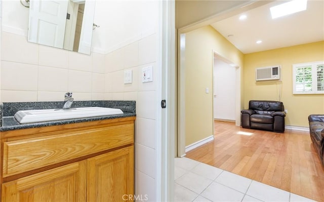 bathroom with vanity, wood finished floors, baseboards, an AC wall unit, and recessed lighting