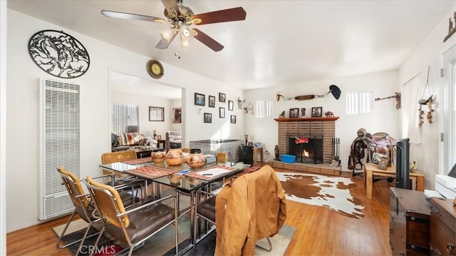 dining space featuring a brick fireplace, a ceiling fan, wood finished floors, and a heating unit