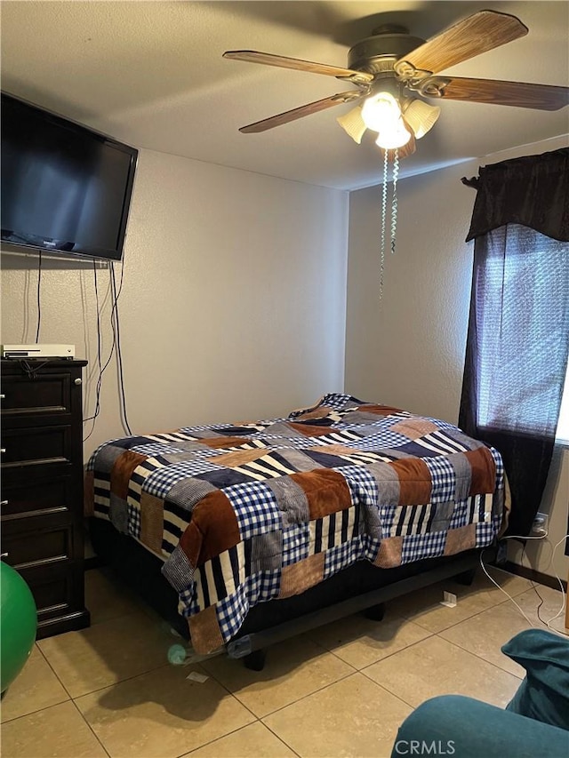 bedroom featuring a ceiling fan, a textured wall, and light tile patterned floors