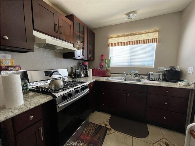 kitchen with a sink, light countertops, gas range, under cabinet range hood, and glass insert cabinets