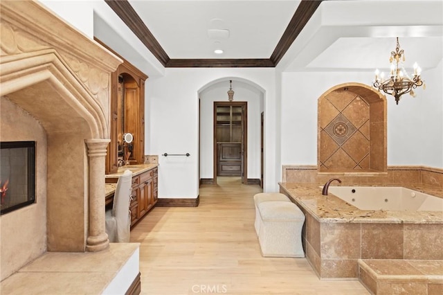 interior space with crown molding, vanity, wood finished floors, a tub with jets, and a notable chandelier