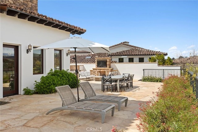 view of patio with an outdoor stone fireplace, outdoor dining area, and fence