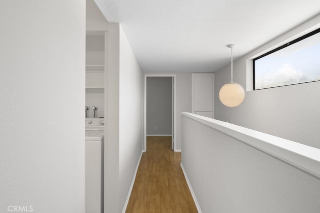 hallway with washer / dryer, wood finished floors, baseboards, a textured ceiling, and an upstairs landing