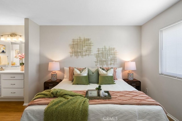 bedroom with baseboards, ensuite bath, and wood finished floors