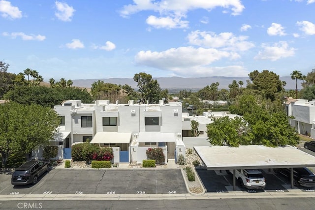 view of building exterior featuring covered and uncovered parking, a residential view, and a mountain view