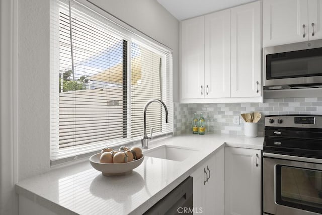 kitchen with decorative backsplash, appliances with stainless steel finishes, a sink, light stone counters, and white cabinets