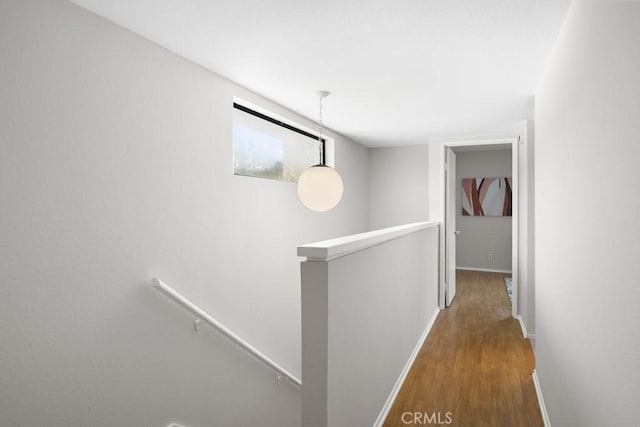corridor featuring baseboards, an upstairs landing, and wood finished floors