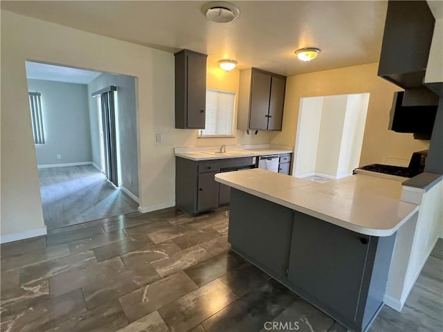 kitchen with a peninsula, baseboards, light countertops, gas range oven, and dishwasher