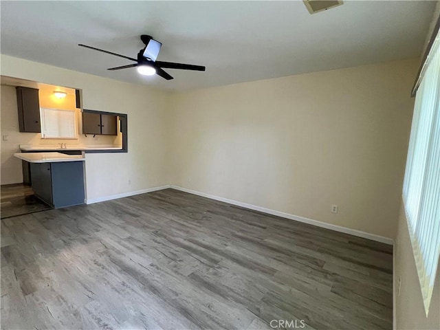 unfurnished living room featuring dark wood-type flooring, baseboards, and ceiling fan