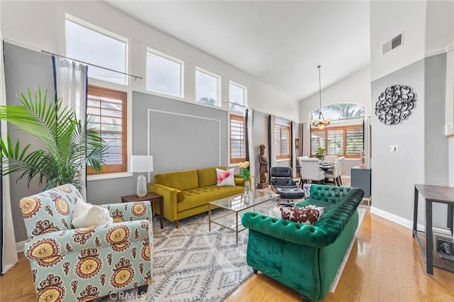 living area featuring visible vents, wood finished floors, a notable chandelier, and high vaulted ceiling