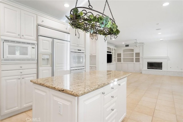 kitchen with built in appliances, a kitchen island, recessed lighting, white cabinets, and light stone counters