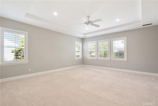 unfurnished room featuring visible vents, baseboards, light colored carpet, a raised ceiling, and a ceiling fan