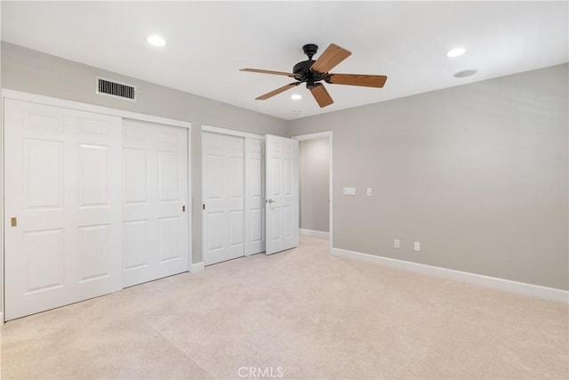 unfurnished bedroom featuring light colored carpet, two closets, recessed lighting, baseboards, and visible vents