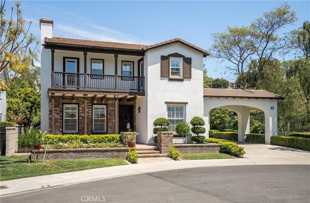 view of front of home with a tile roof, stucco siding, a chimney, a balcony, and driveway