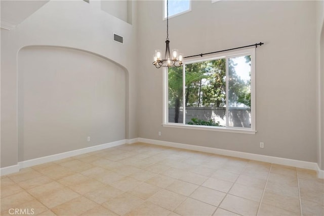 spare room featuring a chandelier, visible vents, a wealth of natural light, and a towering ceiling
