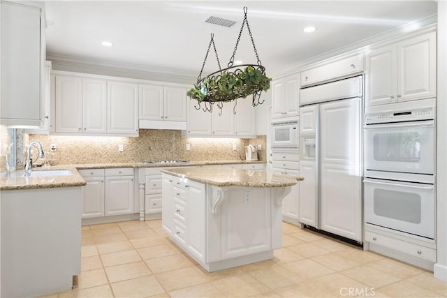 kitchen featuring white cabinets, a sink, built in appliances, backsplash, and visible vents