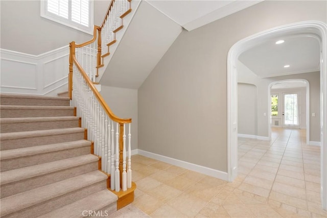 stairway featuring arched walkways, baseboards, tile patterned floors, ornamental molding, and recessed lighting