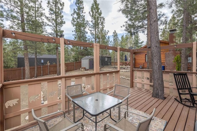 deck featuring a fenced backyard, an outdoor structure, outdoor dining area, and a shed