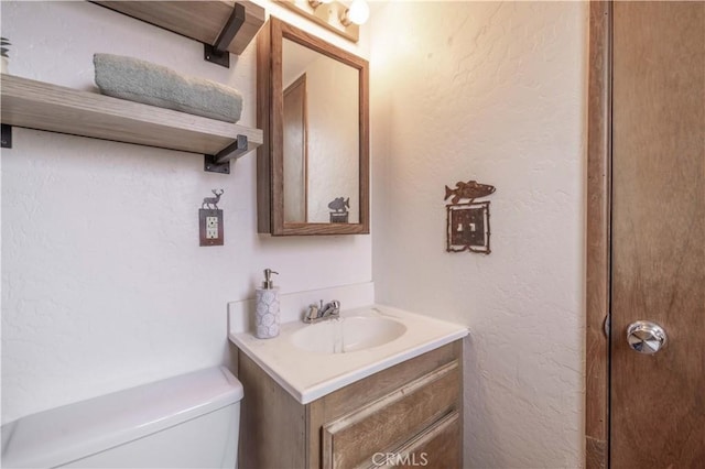half bath featuring toilet, a textured wall, and vanity