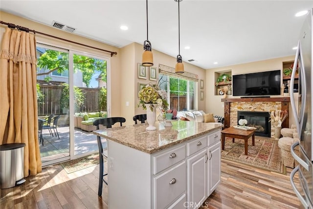 kitchen with a stone fireplace, visible vents, white cabinets, stainless steel fridge, and light wood-style flooring