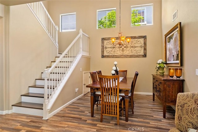 dining room with visible vents, wood finished floors, a notable chandelier, a high ceiling, and stairs