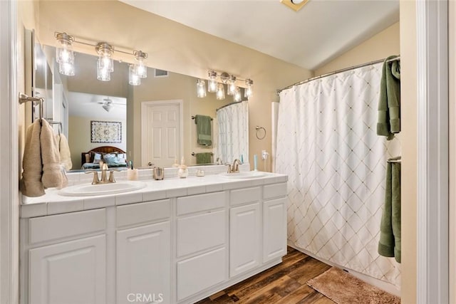 ensuite bathroom featuring double vanity, a sink, lofted ceiling, and wood finished floors