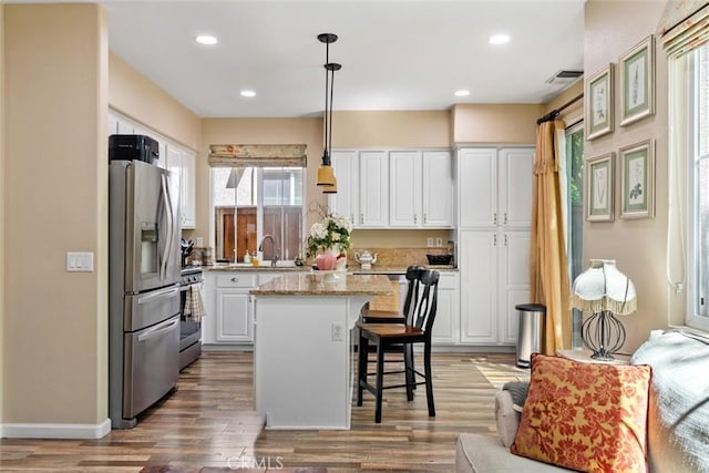 kitchen featuring white cabinets, appliances with stainless steel finishes, a kitchen breakfast bar, wood finished floors, and a kitchen island