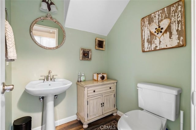 bathroom with a sink, toilet, baseboards, wood finished floors, and vaulted ceiling