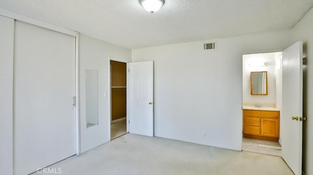 unfurnished bedroom with visible vents, a closet, light carpet, ensuite bathroom, and a textured ceiling