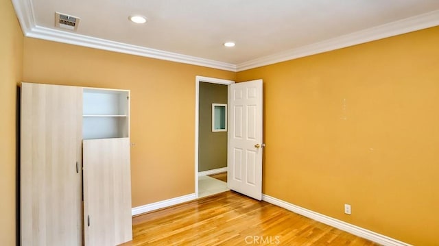 unfurnished bedroom with baseboards, ornamental molding, wood finished floors, and visible vents