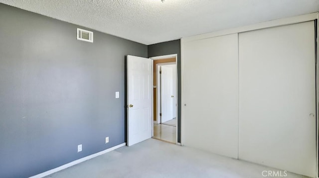 unfurnished bedroom featuring carpet floors, a textured ceiling, visible vents, and a closet