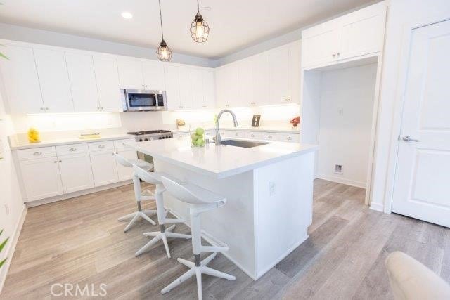 2630 Luminous Ln, Costa Mesa, CA 92626 - kitchen featuring stainless steel microwave, white cabinetry, light wood-type flooring, light countertops, and hanging light fixtures